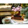 LEGO-Bonsai mit rosa Kirschblüten auf Holzständer, auf Büchern neben einer Teetasse platziert