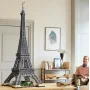 Dunkelgraues LEGO Eiffelturm-Modell mit grüner Basis im modernen Wohnzimmer neben sitzendem Mann