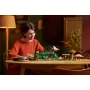 Frau in rotem Pullover baut LEGO Auenland-Set mit Hobbit-Höhlen, Minifiguren und fliegendem Drachen in gemütlichem Wohnzimmer