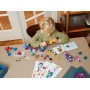 Blondes Kind baut mit bunten LEGO-Steinen am Tisch, mit blau-rotem Spider-Man-Fahrzeug und Bauanleitungen Blondes Kind baut mit bunten LEGO-Steinen am Tisch, mit blau-rotem Spider-Man-Fahrzeug und Bauanleitungen