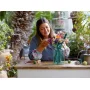 Une femme souriante arrange un bouquet de fleurs LEGO colorées dans un vase sur une table en bois dans un jardin verdoyant Une femme souriante arrange un bouquet de fleurs LEGO colorées dans un vase sur une table en bois dans un jardin verdoyant