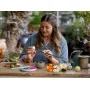 Une femme assemble des fleurs LEGO colorées à une table en bois avec des pièces éparses et un arrosoir vert Une femme assemble des fleurs LEGO colorées à une table en bois avec des pièces éparses et un arrosoir vert