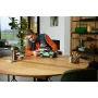 Homme assemblant le modèle LEGO Land Rover Defender 90 vert sur une table en bois dans un salon moderne