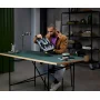 Homme en veste marron consultant le manuel d'instructions LEGO à un bureau dans un environnement moderne