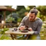 Man building the LEGO bonsai tree at a garden table, with the miniature tree featuring green leaves visible beside him