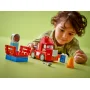 Child playing with red LEGO Mack truck and racing trailer, with orange cone and accessories on green background