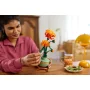 Woman gently holding an orange and red LEGO chrysanthemum in a green pot on a wooden table