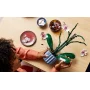Hands building a LEGO orchid with pink flowers and green leaves on wooden table with decorative bowls and scattered petals