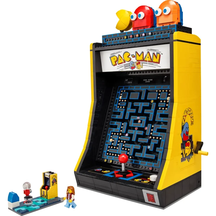 Máquina recreativa LEGO PAC-MAN amarilla con pantalla de juego, figuras coloridas arriba y minifiguras LEGO al lado