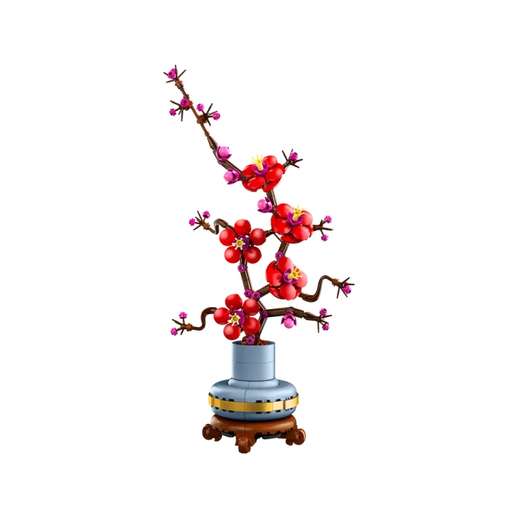 Rama de ciruelo LEGO con flores rojas y capullos rosas en jarrón azul y amarillo sobre base de madera