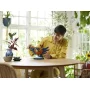 Hombre con camisa amarilla construyendo martín pescador LEGO con alas extendidas en mesa de madera junto a ventana