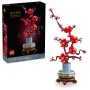 Rama de ciruelo LEGO con flores rojas y capullos violetas en jarrón gris sobre base de madera, junto a su caja negra