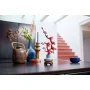 Rama de ciruelo LEGO con flores rosas en jarrón azul sobre mesa, rodeada de objetos decorativos en interior moderno