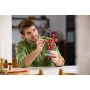 Hombre sonriente con camisa verde sosteniendo cuidadosamente el modelo LEGO de flores de ciruelo rosa y rojas en cocina moderna