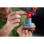 Manos sosteniendo delicadamente un jarrón LEGO azul y marrón con flores de ciruelo rosas y rojas construidas con ladrillos LEGO