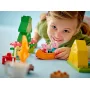 Niño sonriente jugando con set LEGO de camping, sosteniendo canoa naranja con figuras de Peppa Pig, tienda amarilla y árbol verde