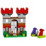 Castello LEGO con torri rosse, ingresso con cancello e base verde, accanto a due piccole case colorate