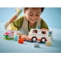Kind speelt met witte en oranje LEGO ambulance, poppetjes in voertuig, kleurrijke blokjes en huis op de achtergrond