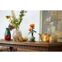 Oranje en rode LEGO chrysant in groene vaas op houten console, omringd door echte bloemen en decoratieve objecten Oranje en rode LEGO chrysant in groene vaas op houten console, omringd door echte bloemen en decoratieve objecten