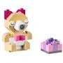 Beige LEGO puppy met grijze neus en roze tong naast een kleine veelkleurige roze en paarse taart