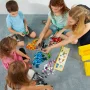 Familie bouwt samen met kleurrijke LEGO-stenen verspreid op tapijt, instructieboekje zichtbaar