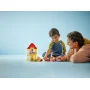 Een kind en volwassene spelen samen met de LEGO Peppa Pig set, met geel huis met rood dak en kleurrijke poppetjes
